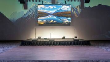 Eine Präsentationsbühne mit einer großen Leinwand, die eine Berglandschaft zeigt, einem Rednerpult und einem Mikrofonständer.