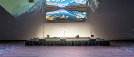 Een presentatiepodium met een groot scherm waarop een berglandschap wordt getoond, een spreekgestalte en een microfoonstandaard.