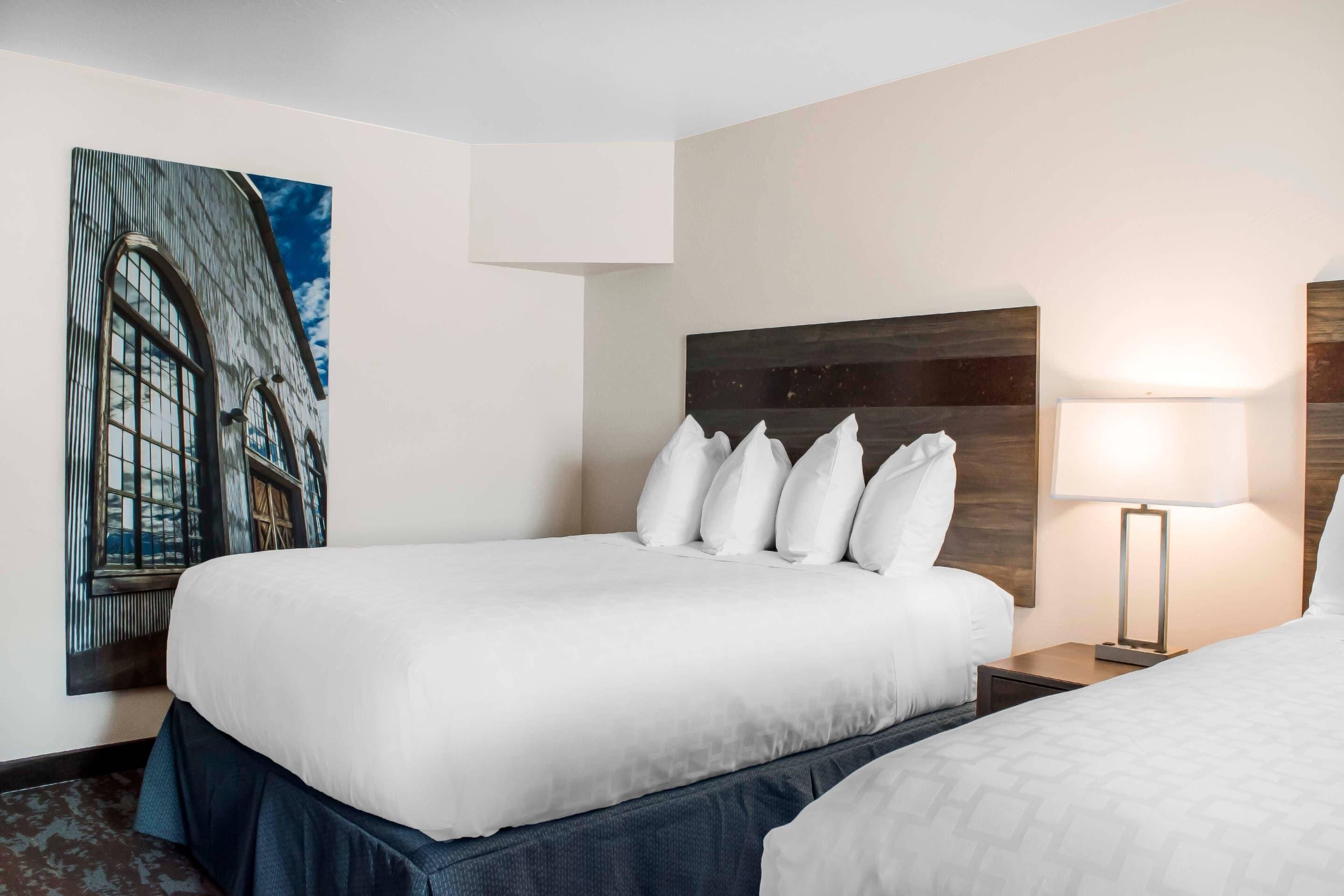 A hotel room with a large bed, a nightstand with a lamp, and a wall-mounted artwork.