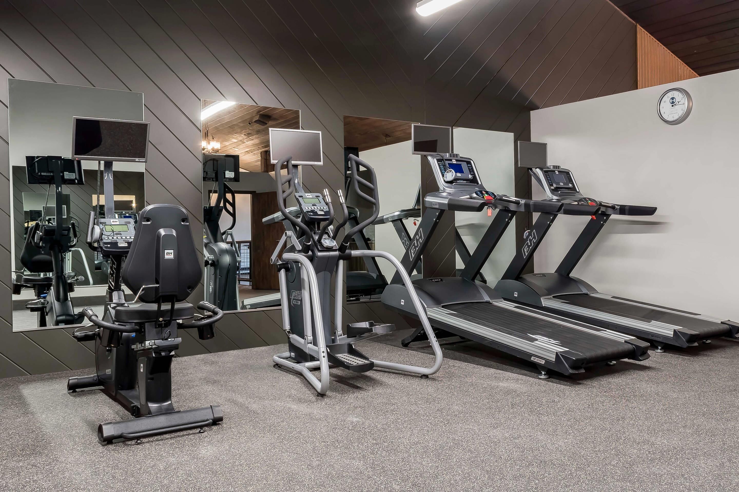 Un gimnasio con cintas de correr, una elíptica y una bicicleta estática.