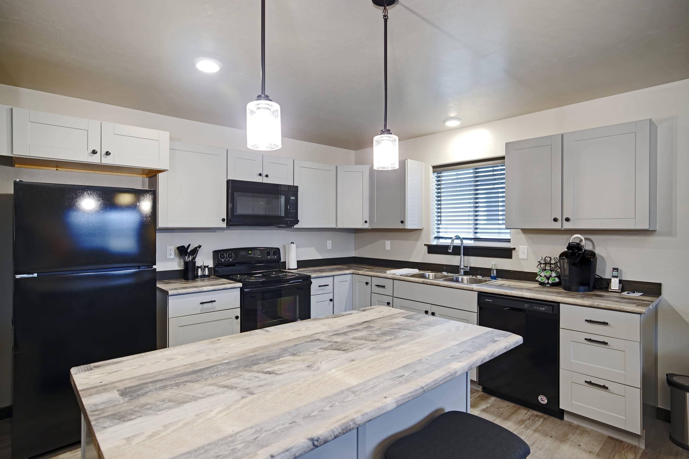 A modern kitchen with white cabinets, a black refrigerator, a microwave, a stove, and a dishwasher. There are pendant lights hanging from the ceiling.