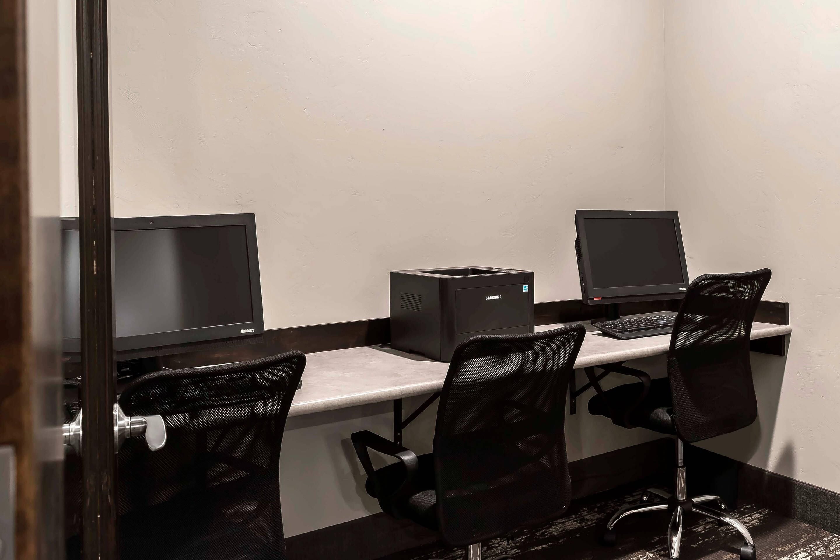 A small office space with two desks, each with a computer monitor, a keyboard, and a chair.