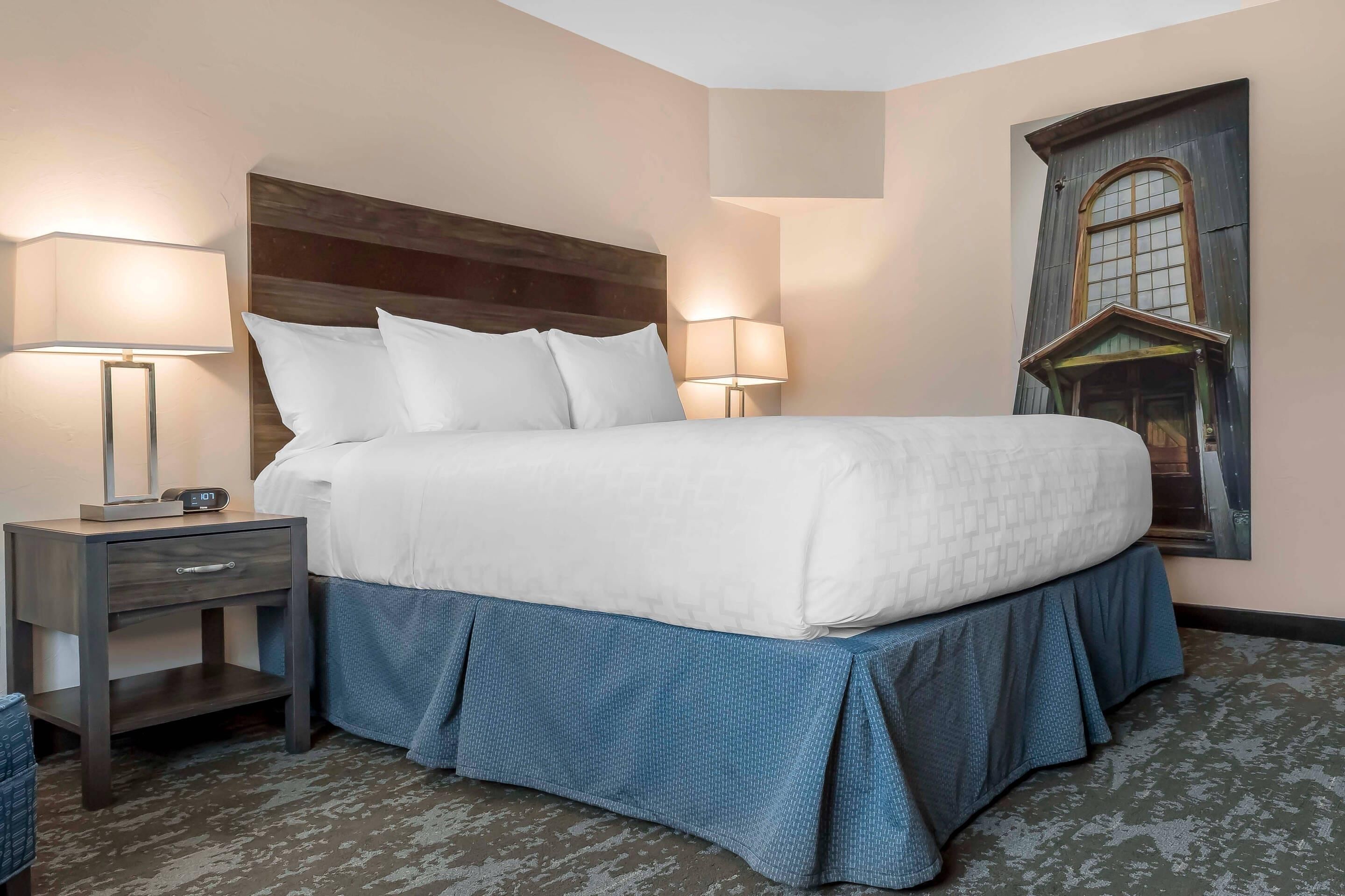 A neatly made bed with a wooden headboard, two bedside tables with lamps, and a wall-mounted picture of a window.