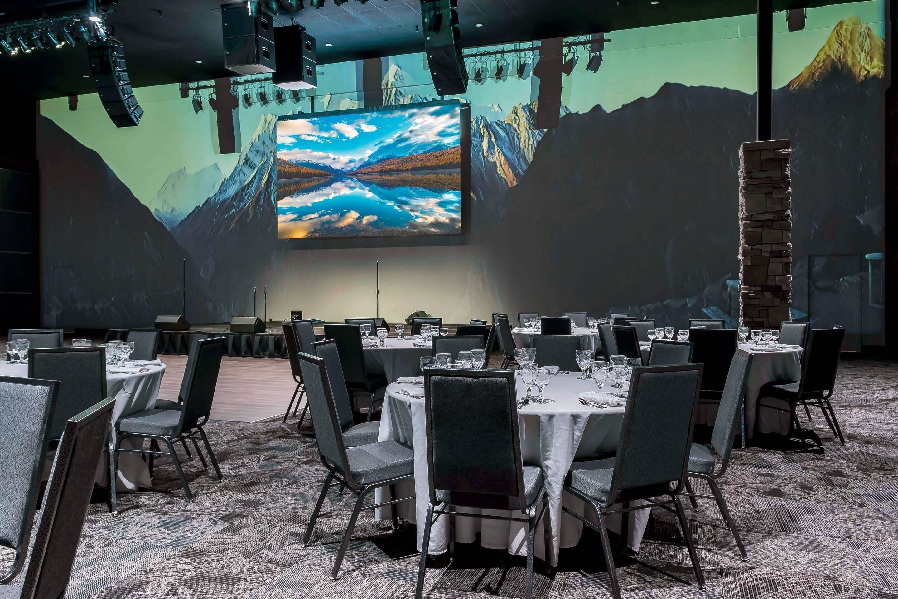 Une salle de conférence équipée de tables rondes, de chaises et d’un grand écran diffusant un paysage de montagne.