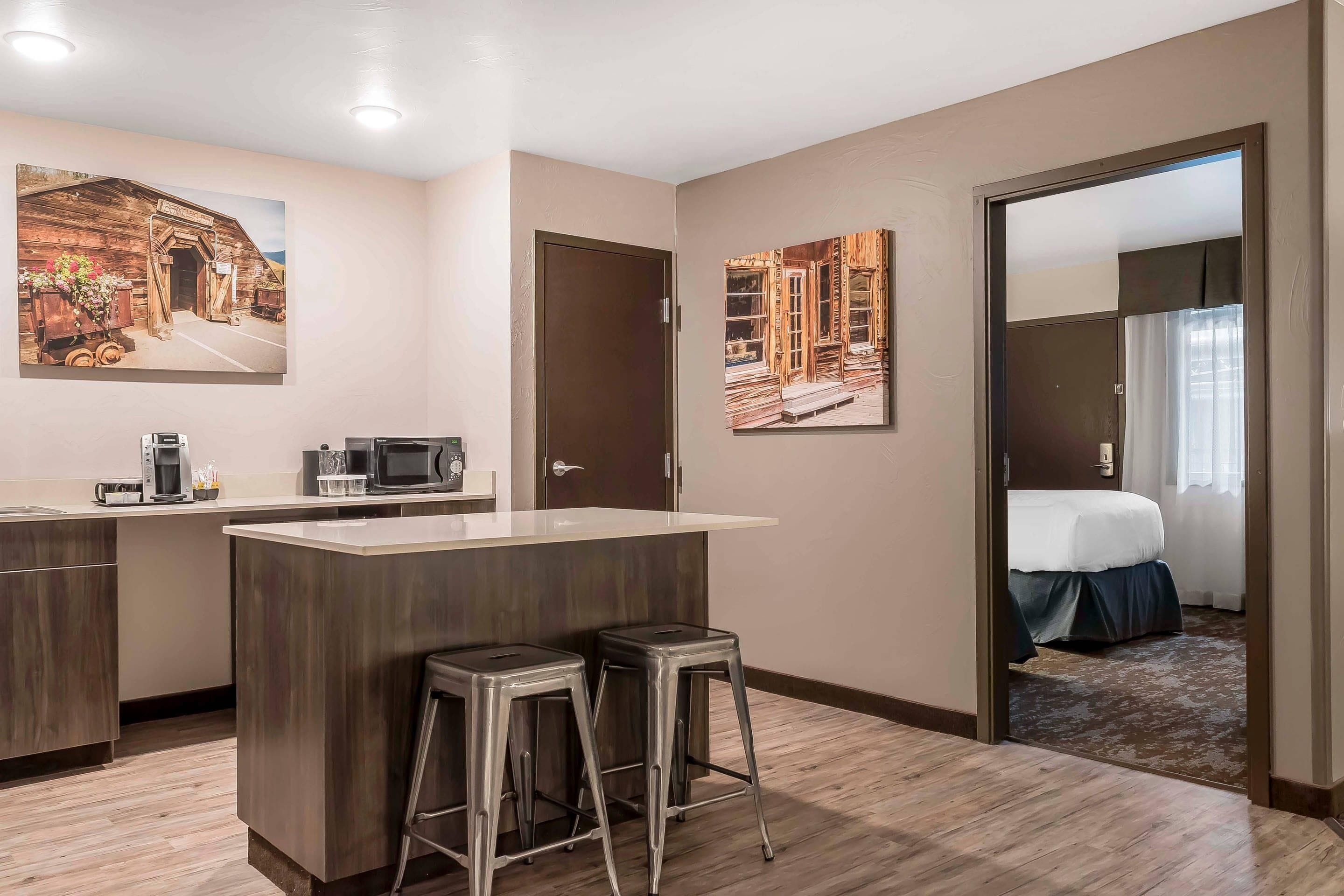 A hotel room with a kitchenette, a bed, and two barstools.