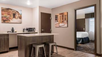 A hotel room with a kitchenette, a bed, and two barstools.