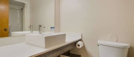 Un baño con lavamanos blanco, estante de madera, inodoro y espejo.