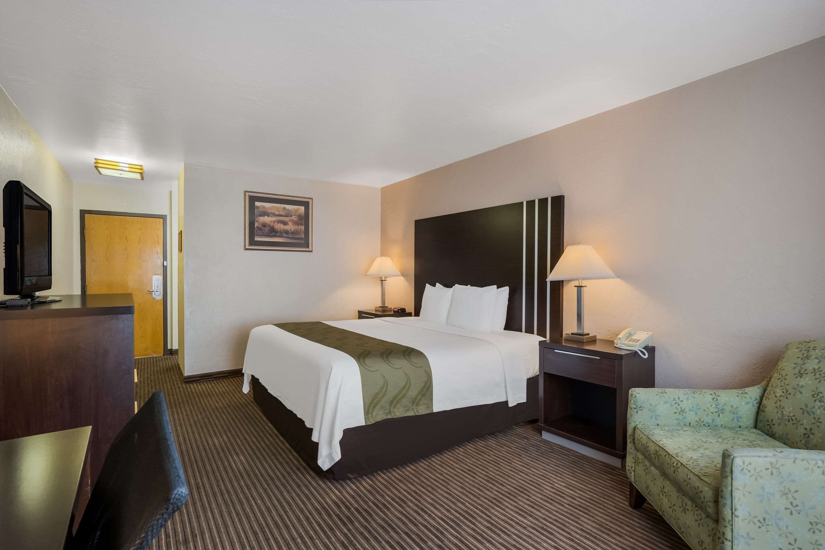 A hotel room with a bed, two bedside lamps, a desk with a telephone, a television, and a chair.