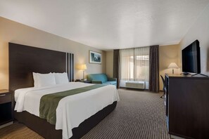 A hotel room with a large bed, a desk with a TV, a chair, and a window with curtains.