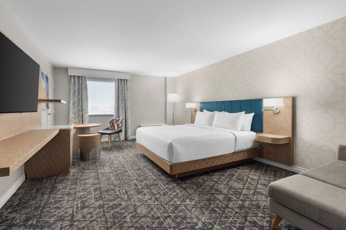 A hotel room with a bed, bedside tables, a desk, a chair, and a TV.