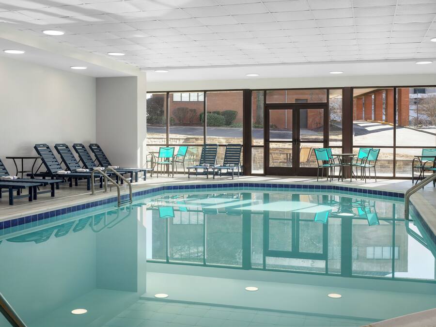 Una piscina interior amb parets de vidre transparent, diverses gandules i taules.
