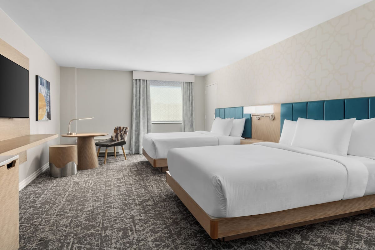 A hotel room with two beds, a desk, a chair, a TV, and a window with curtains.