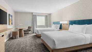 A hotel room with two beds, a desk, a chair, a TV, and a window with curtains.