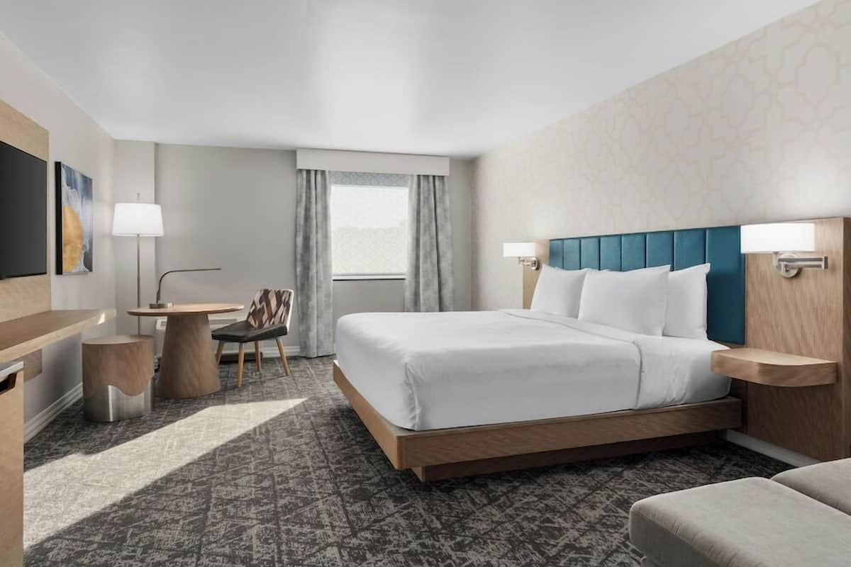 A hotel room with a bed, bedside tables, a desk, a chair, and a TV.