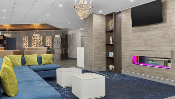 A modern living room with a sectional sofa, white ottomans, a chandelier, a flat-screen TV, and a fireplace with a pink light. - DoubleTree by Hilton Salisbury (Salisbury)