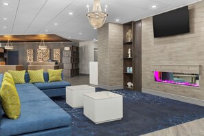 A modern living room with a sectional sofa, white ottomans, a chandelier, a flat-screen TV, and a fireplace with a pink light. - DoubleTree by Hilton Salisbury (Salisbury)