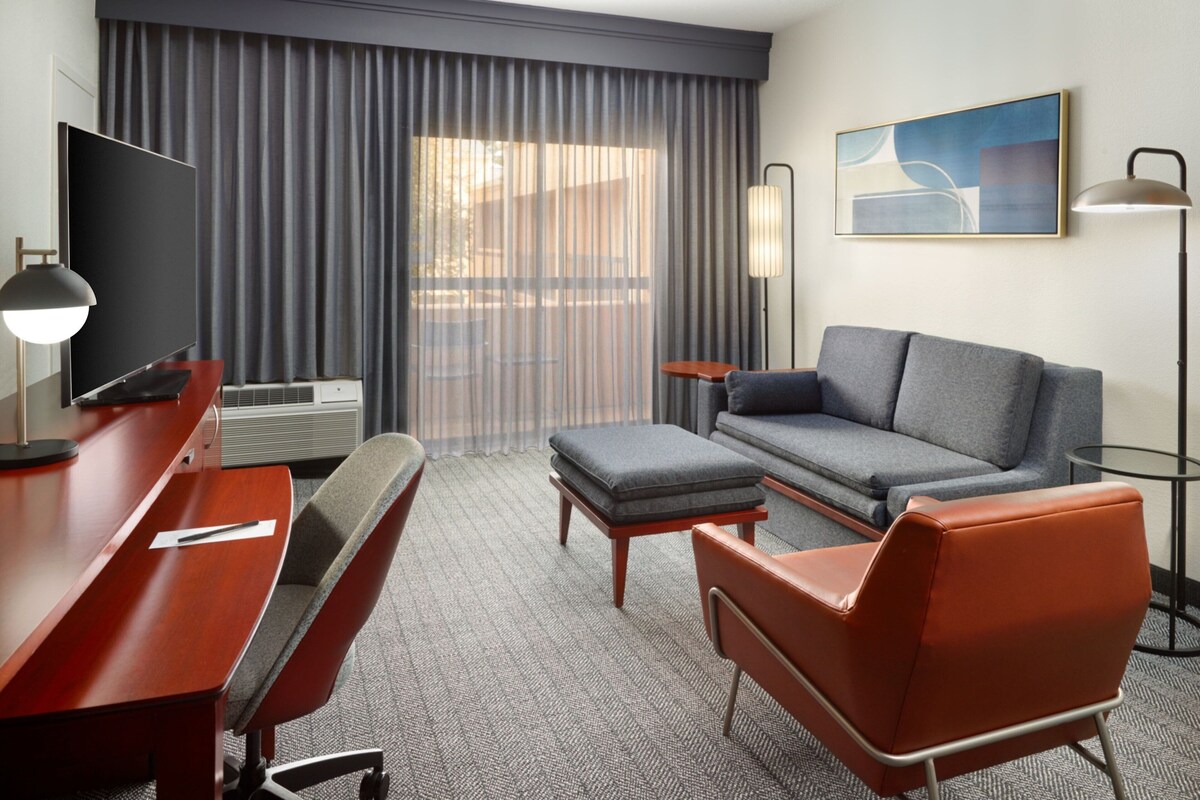 A hotel room with a flat-screen TV, a sofa, a chair, a desk, and a lamp.