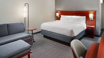 A hotel room with a bed, a sofa, a chair, a small table, and a floor lamp.