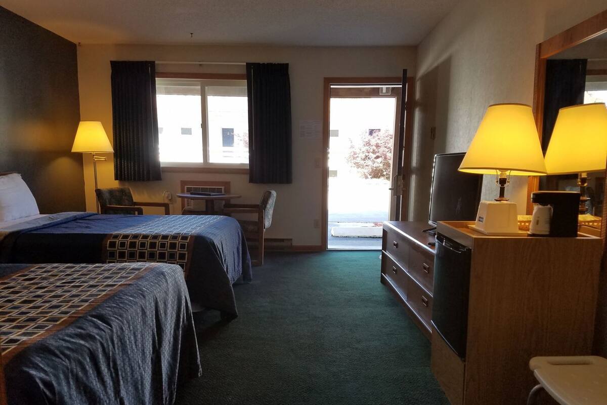 Ein Hotelzimmer mit zwei Betten, einem Schreibtisch, einem Stuhl, einem Fernseher und einer Kaffeemaschine.