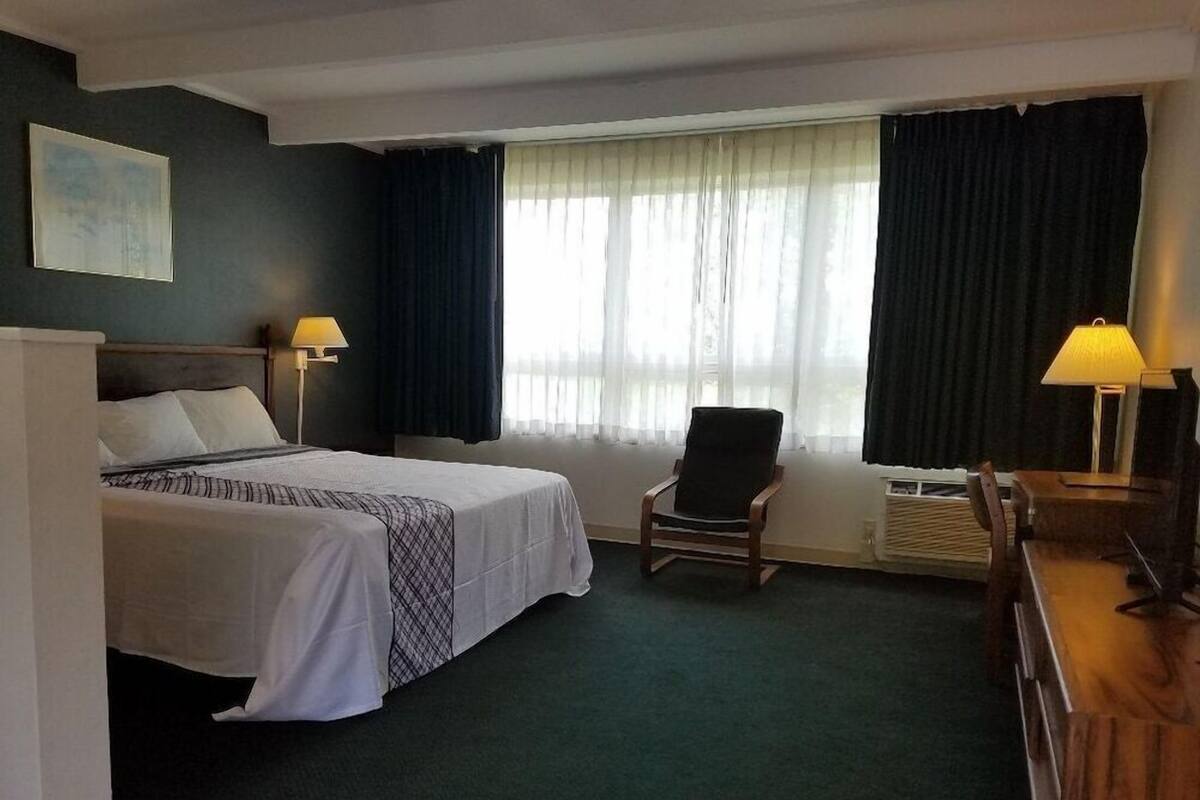 Ein Hotelzimmer mit Bett, Stuhl, Schreibtisch und einem Fenster mit Vorhängen.