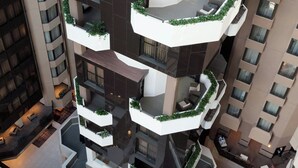 A multi-story hotel with a unique circular rooftop terrace, multiple balconies with greenery, and a modern interior design.