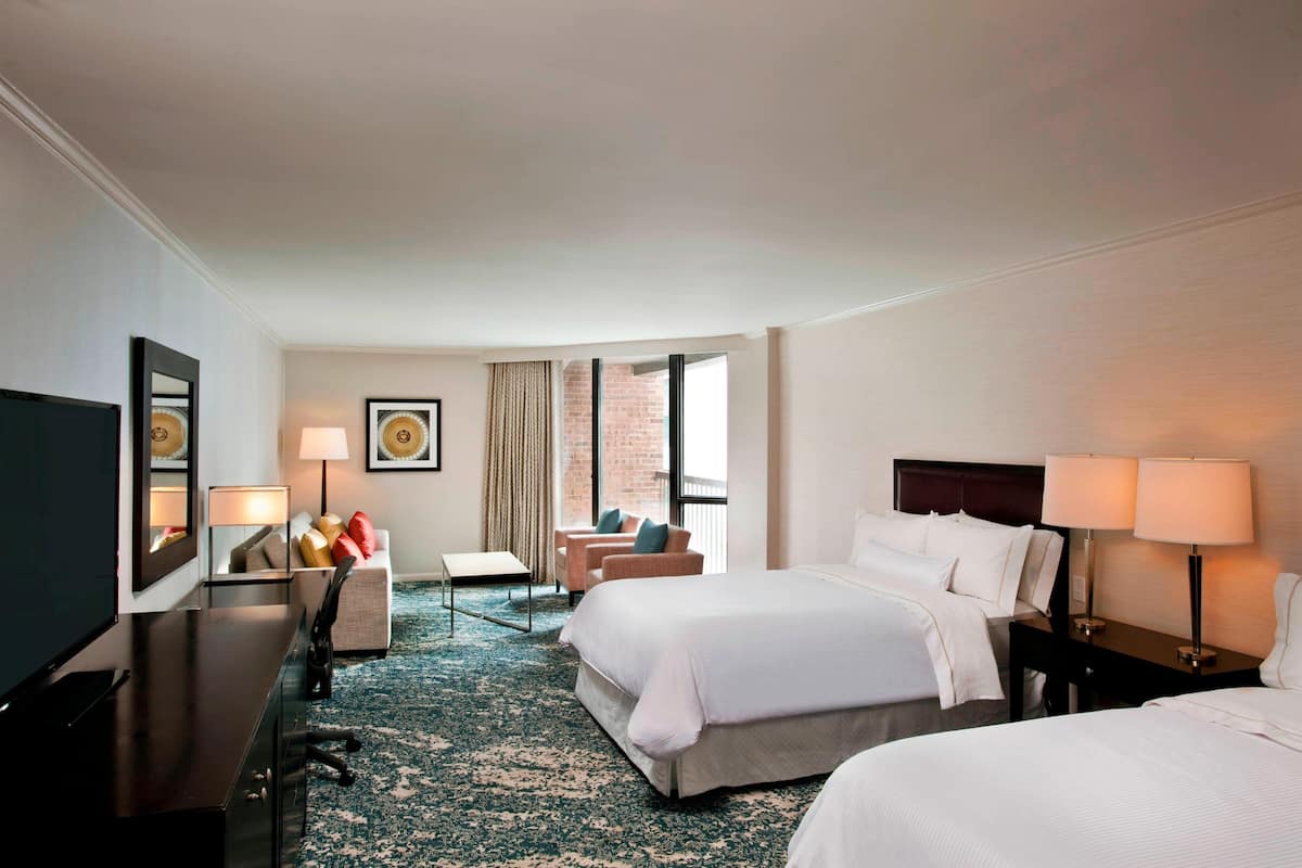 A hotel room with two beds, a desk, a chair, a TV, and a window with curtains.