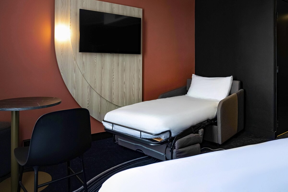 Una habitación de hotel compacta con una cama individual, una mesita pequeña y una silla.