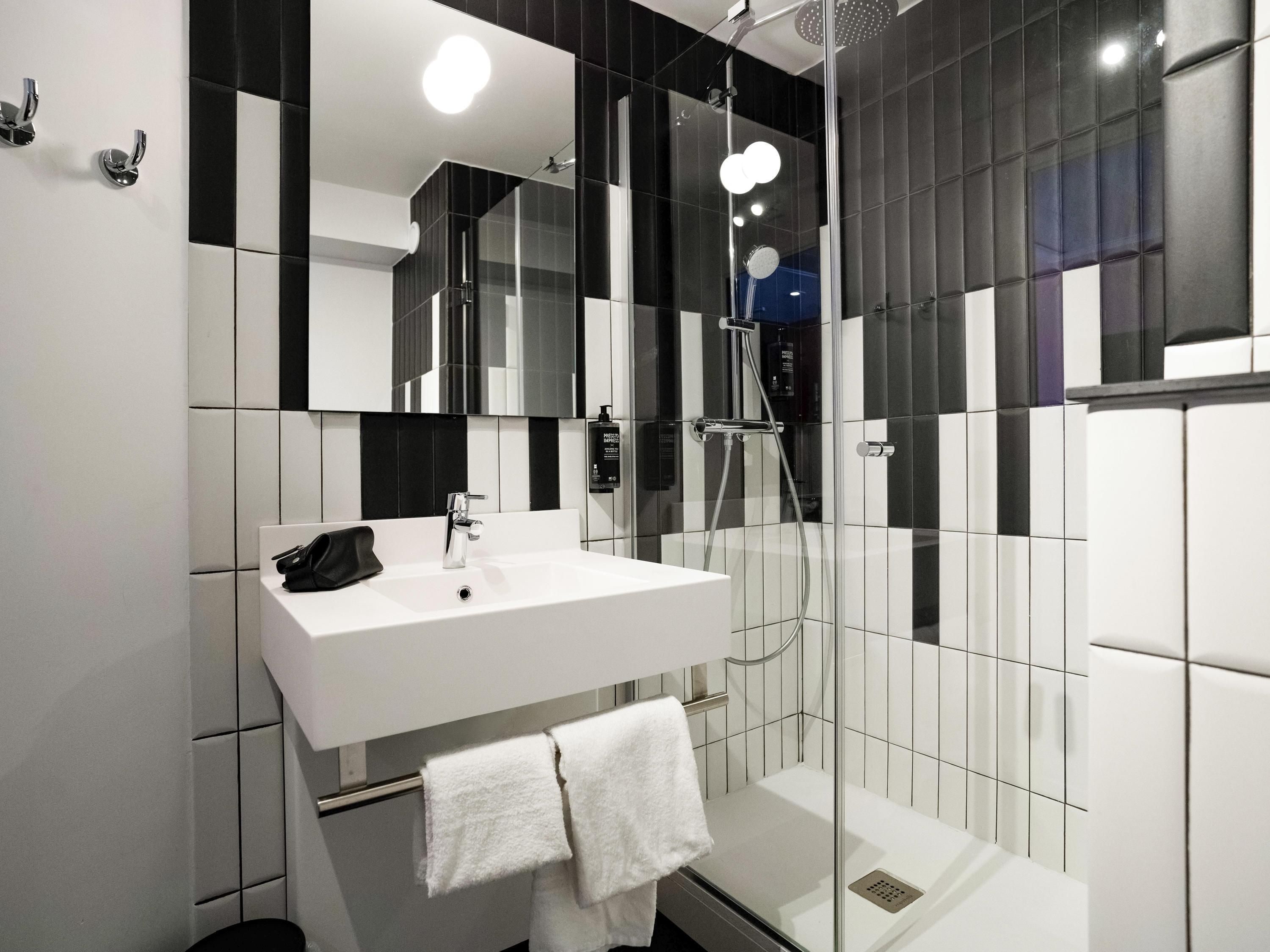 A modern bathroom with a white sink, black and white tiles, a glass shower enclosure, and a mirror above the sink.