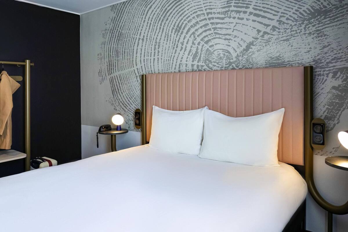 Ein Hotelzimmer mit einem großen Bett, zwei Nachttischen mit Lampen, einem Kleiderständer und einer Wand mit Strukturmuster.