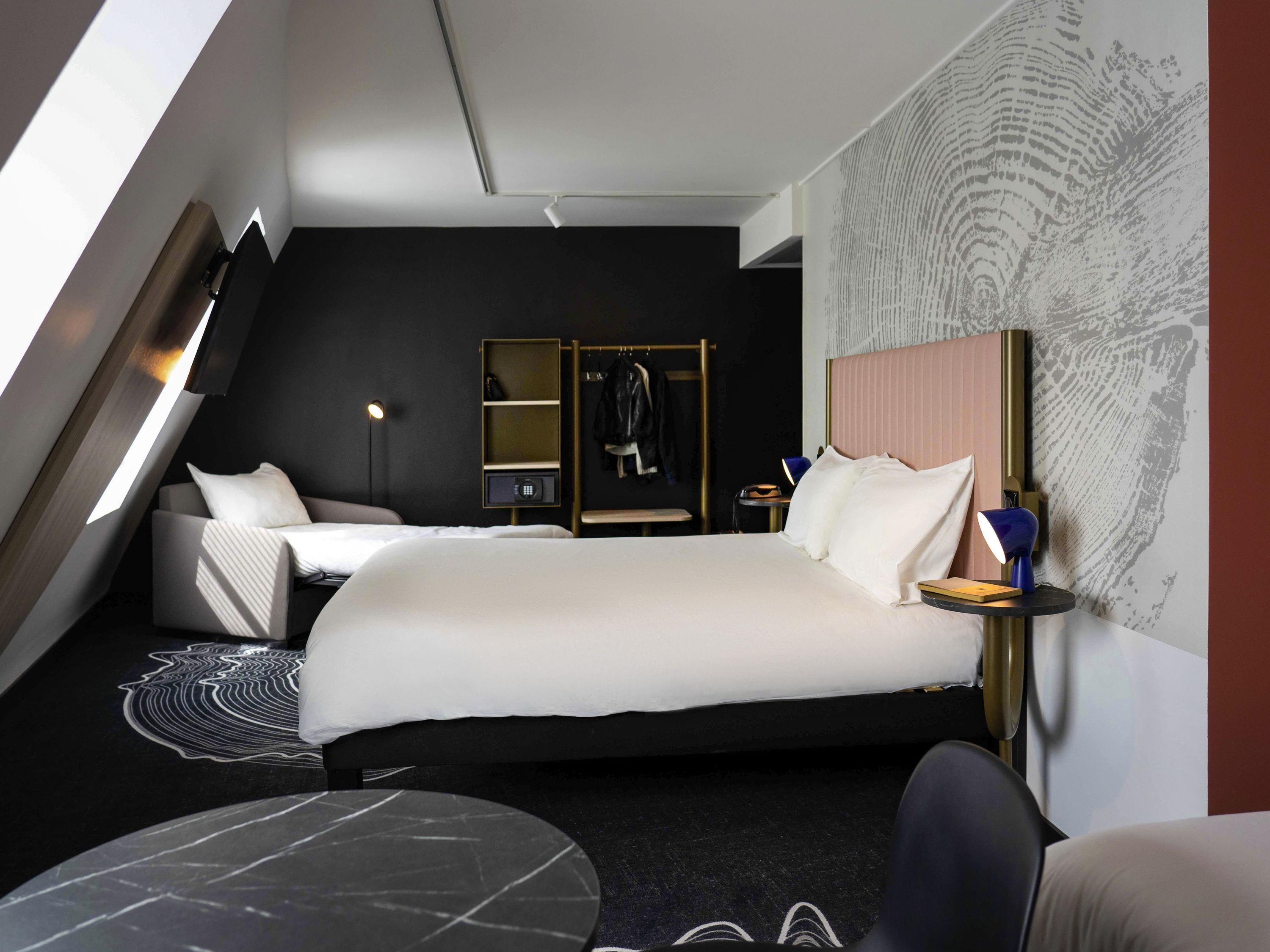 A modern hotel room with a large bed, a desk, a chair, and a small round table.