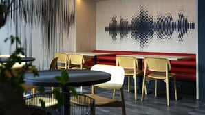 A modern restaurant interior with wooden chairs, a red booth, and a wall with a sound wave pattern. - ibis Styles Paris Porte de Versailles - Mairie d'Issy (Issy-les-Moulineaux)