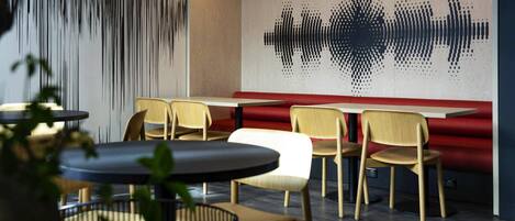 A modern restaurant interior with wooden chairs, a red booth, and a wall with a sound wave pattern.