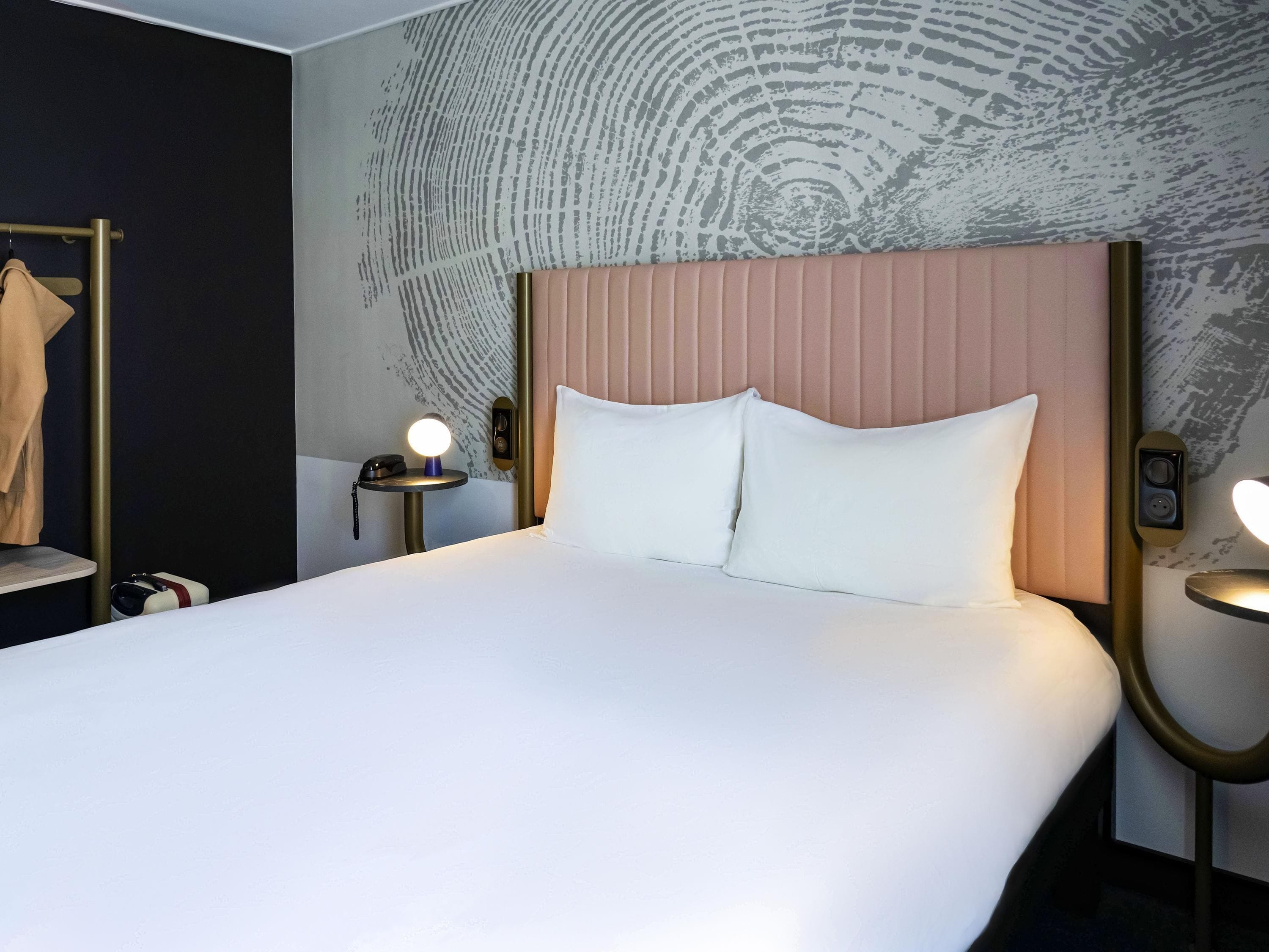 A hotel room with a large bed, two bedside tables with lamps, a coat rack, and a wall with a textured pattern.