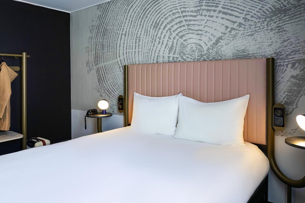 Una habitación de hotel con una cama grande, dos mesitas de noche con lámparas, un perchero y una pared con textura.