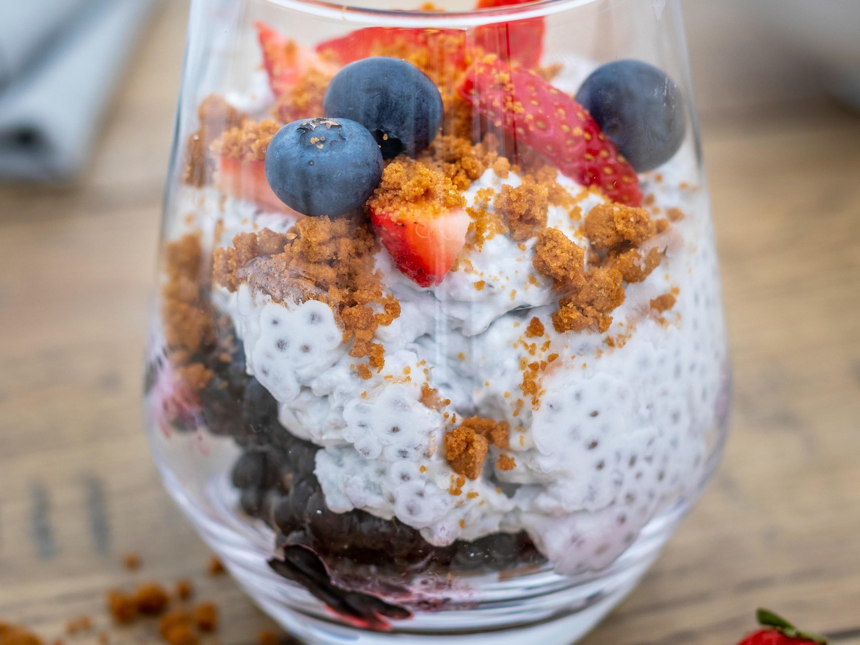 Un dessert servi dans un verre transparent, avec des couches bien distinctes de yaourt, de granola, de fraises et de myrtilles.
