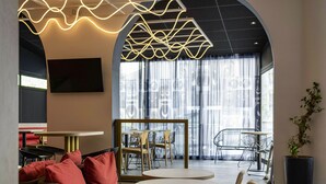 A modern interior with a curved wall, a seating area with red cushions, a round table, and a large potted plant. - ibis Styles Paris Porte de Versailles - Mairie d'Issy (Issy-les-Moulineaux)