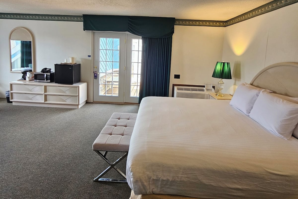 Une chambre d’hôtel avec un grand lit, un bureau avec un ordinateur, une chaise et une fenêtre avec des rideaux.