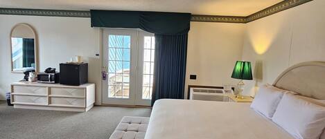 Habitación de hotel con una cama grande, un escritorio con computadora, una silla y un ventanal con cortinas.
