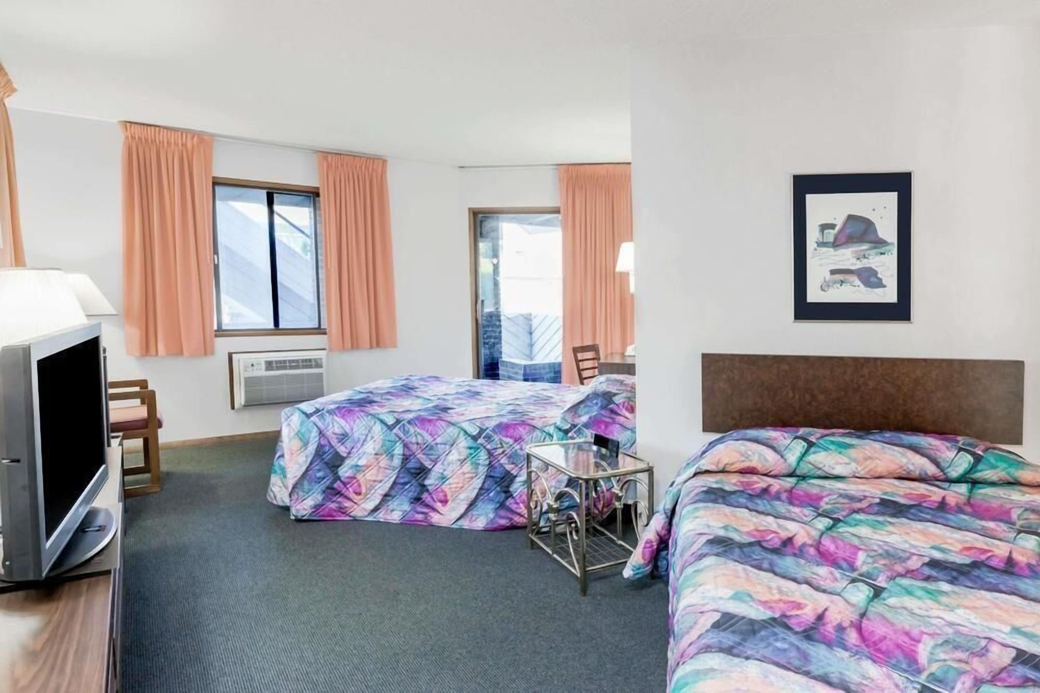 A hotel room with two beds, a television, a desk, and a window with curtains.
