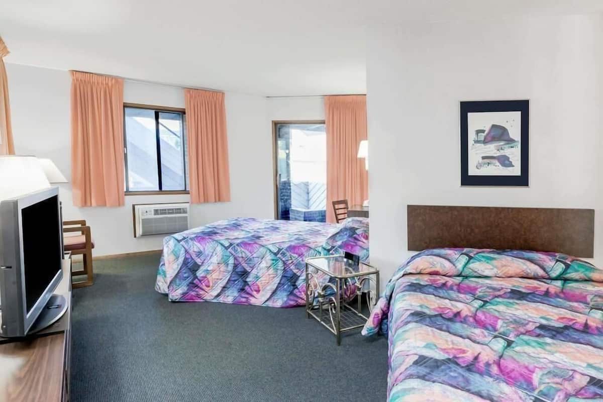 Une chambre d’hôtel avec deux lits, une télévision, un bureau et une fenêtre avec des rideaux.
