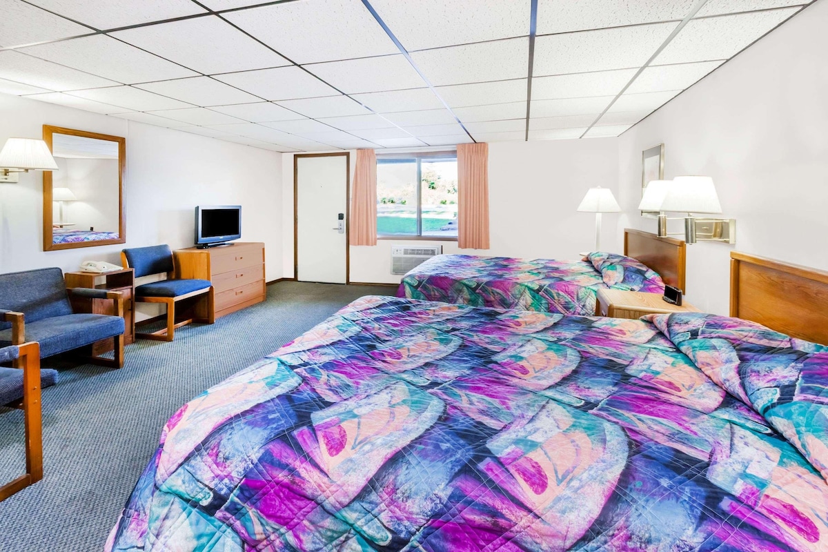 Une chambre d’hôtel avec deux lits, une télévision, un bureau et une fenêtre donnant sur l’extérieur.