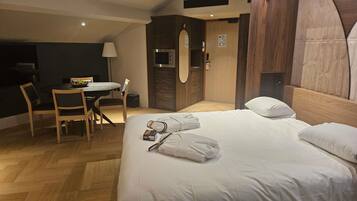 A hotel room with a bed, a desk, a chair, and a small table with a bowl of fruit.