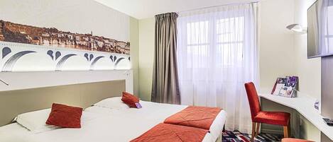 Habitación de hotel con cama, escritorio, silla, televisor y vista a la ciudad.