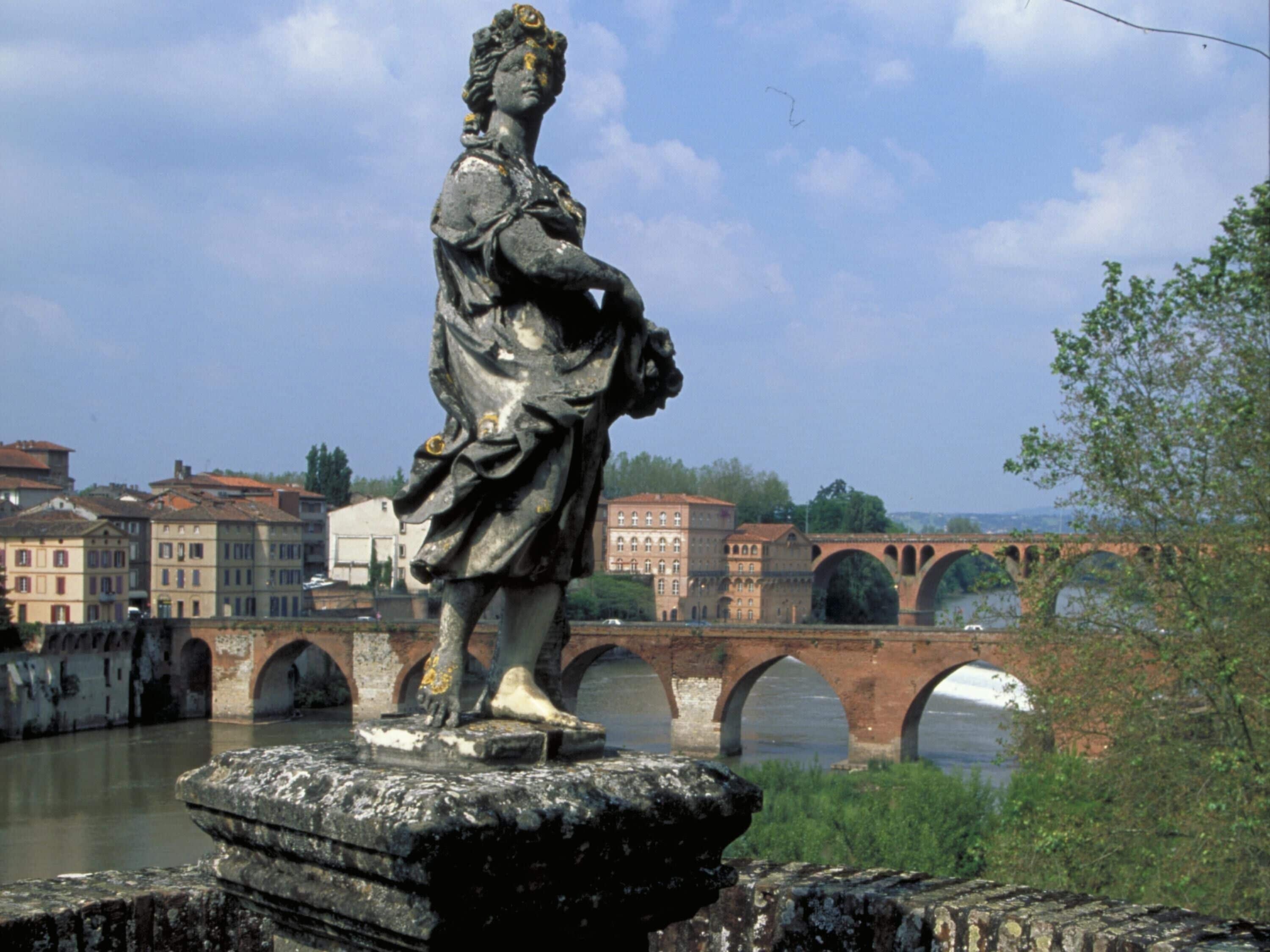 A statue on a pedestal with a bridge and buildings in the background.
