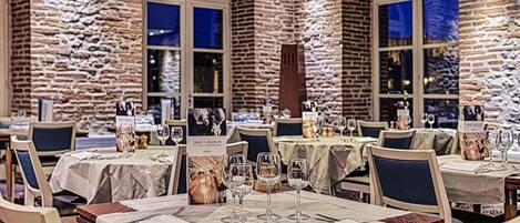 Un restaurante con paredes de piedra y ventanas arqueadas, mesas dispuestas con copas de vino y menús.