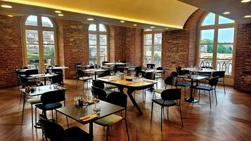 Un restaurante con paredes de ladrillo, ventanas amplias y suelo de madera. Las mesas están dispuestas con sillas y copas de vino.