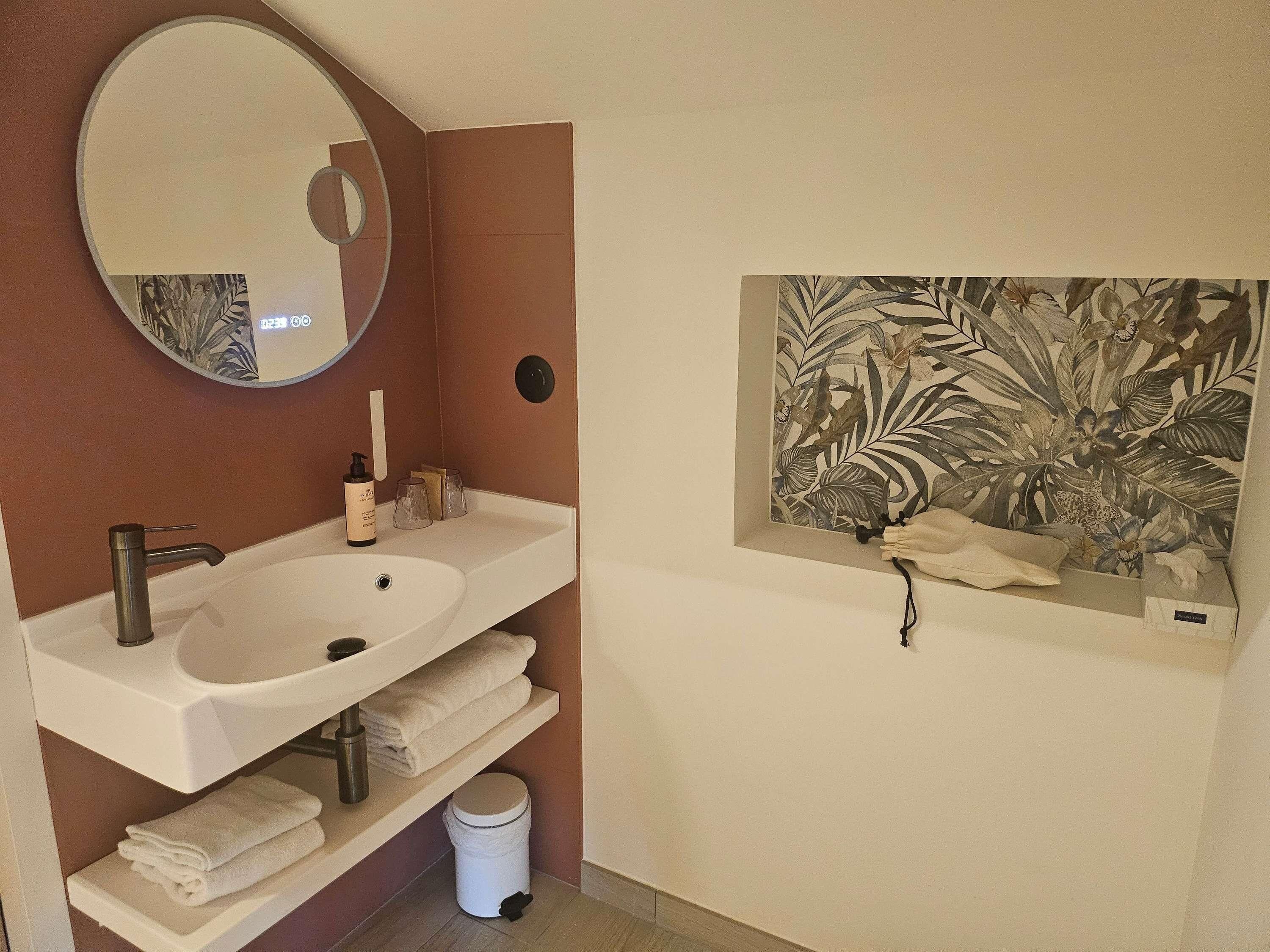 Un baño con un lavamanos blanco, un espejo redondo y un perchero para toallas en la pared.