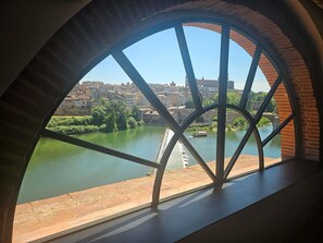 A view through a large arched window overlooking a river, a bridge, and a cityscape.