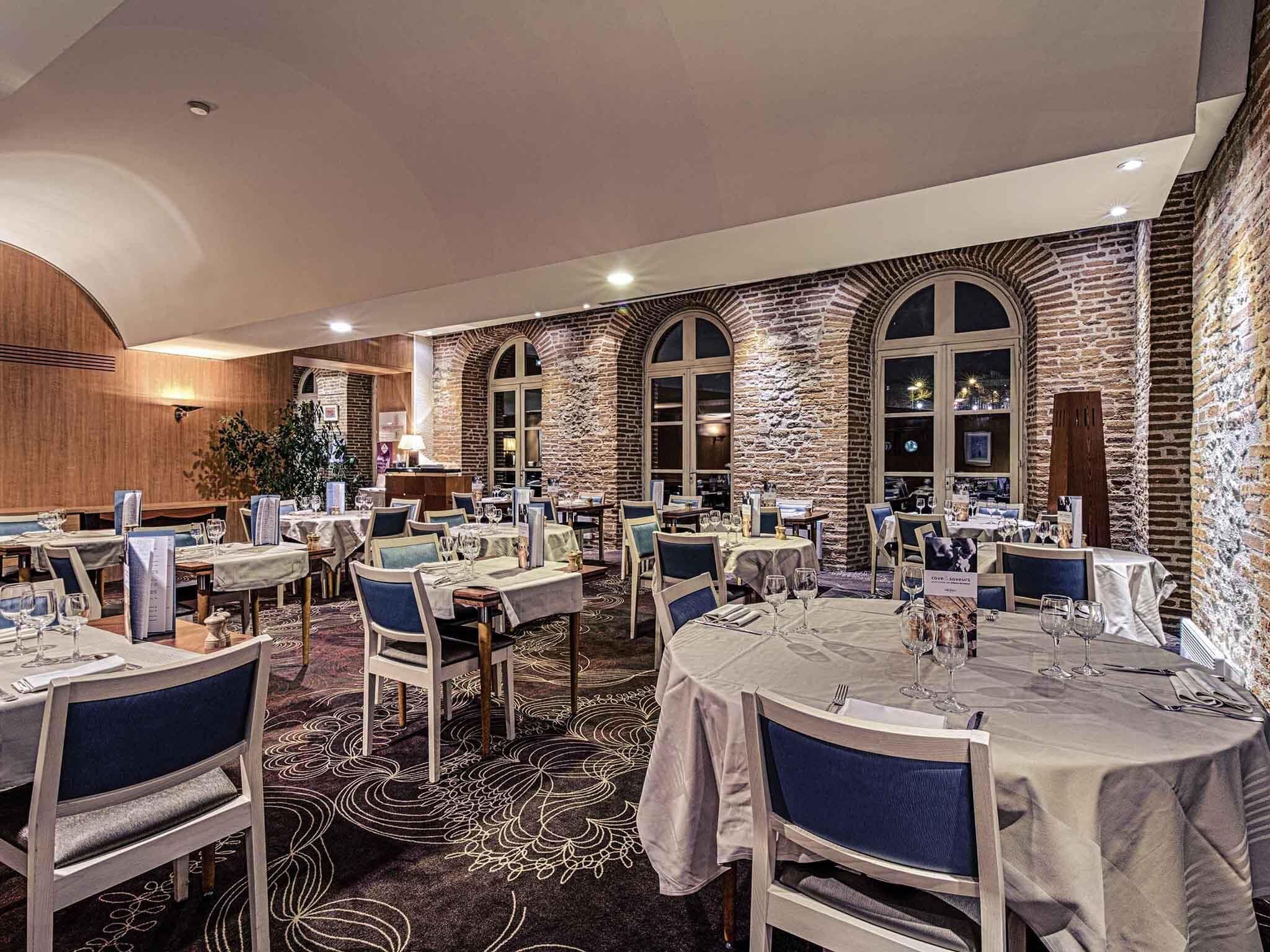 A restaurant with multiple tables, chairs, and a stone wall.