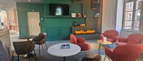 A modern lounge area with red and brown chairs, a flat-screen TV, and a fireplace.